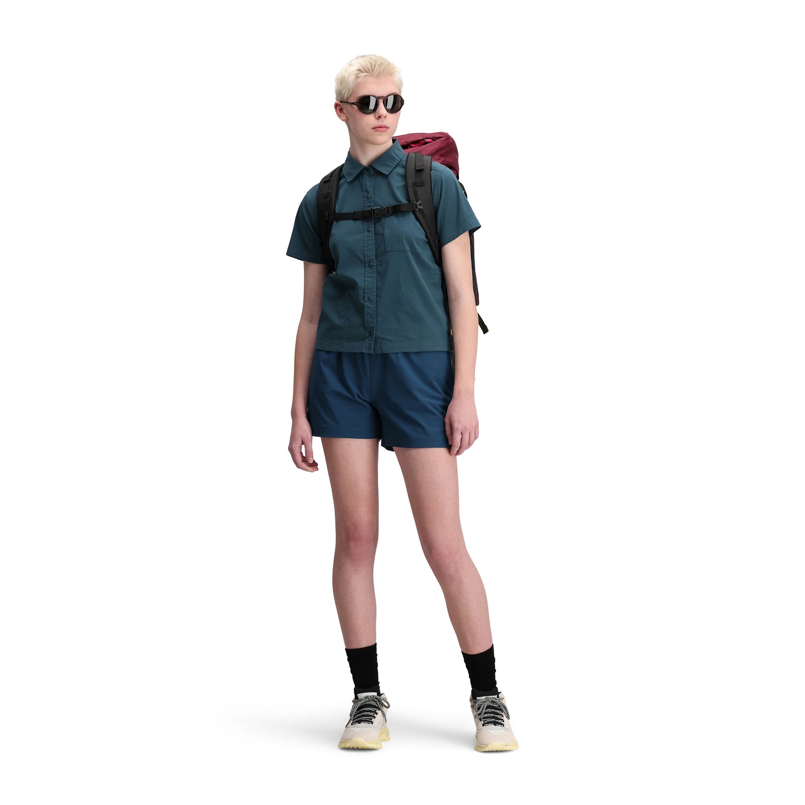  Front model shot of Topo Designs Women's Global Shirt Short Sleeve 30+ UPF rated travel shirt in "Pond Blue" green. Show on "brick".