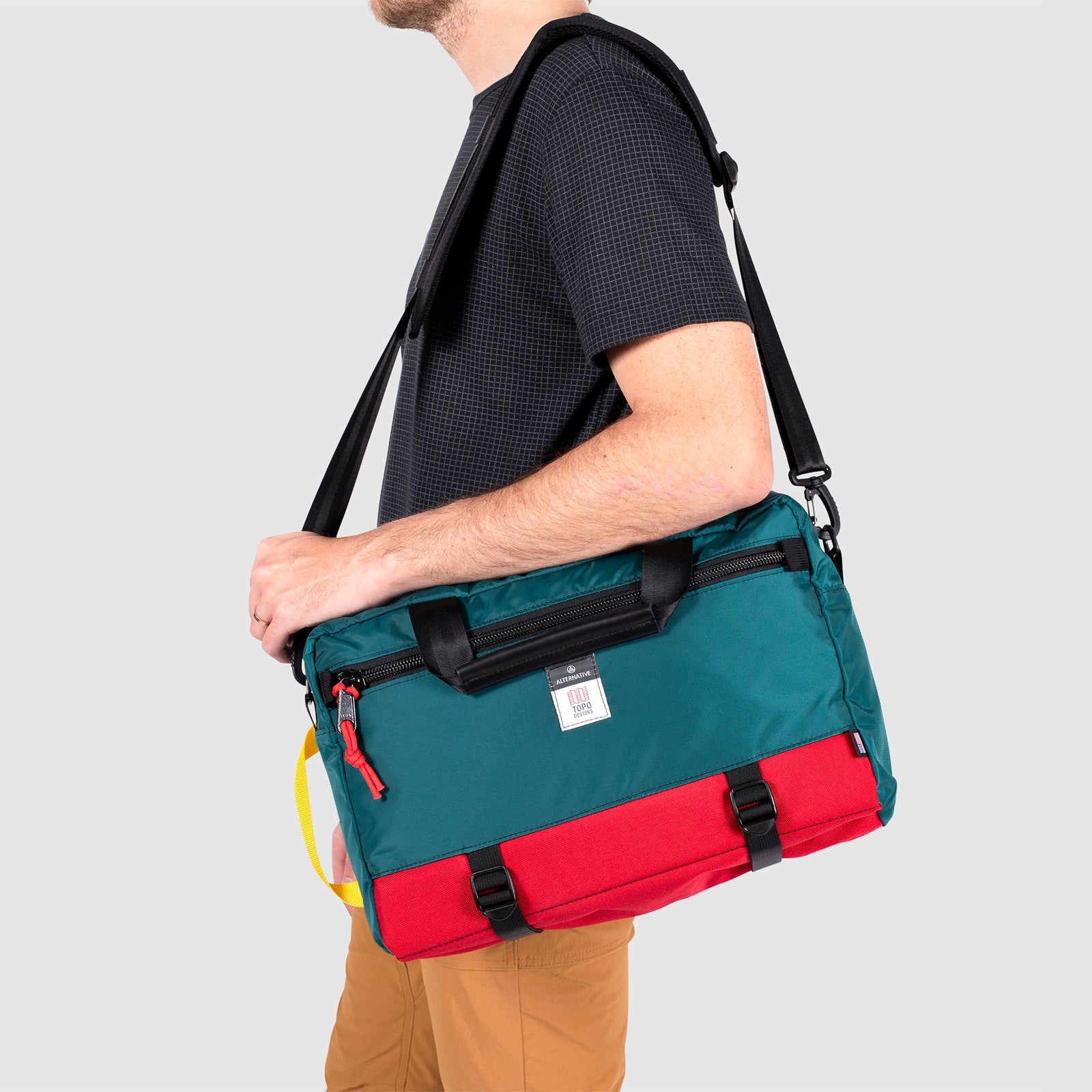 Close-up model shot of Topo Designs x Alternative Commuter Briefcase in red/teal showing shoulder strap carry style