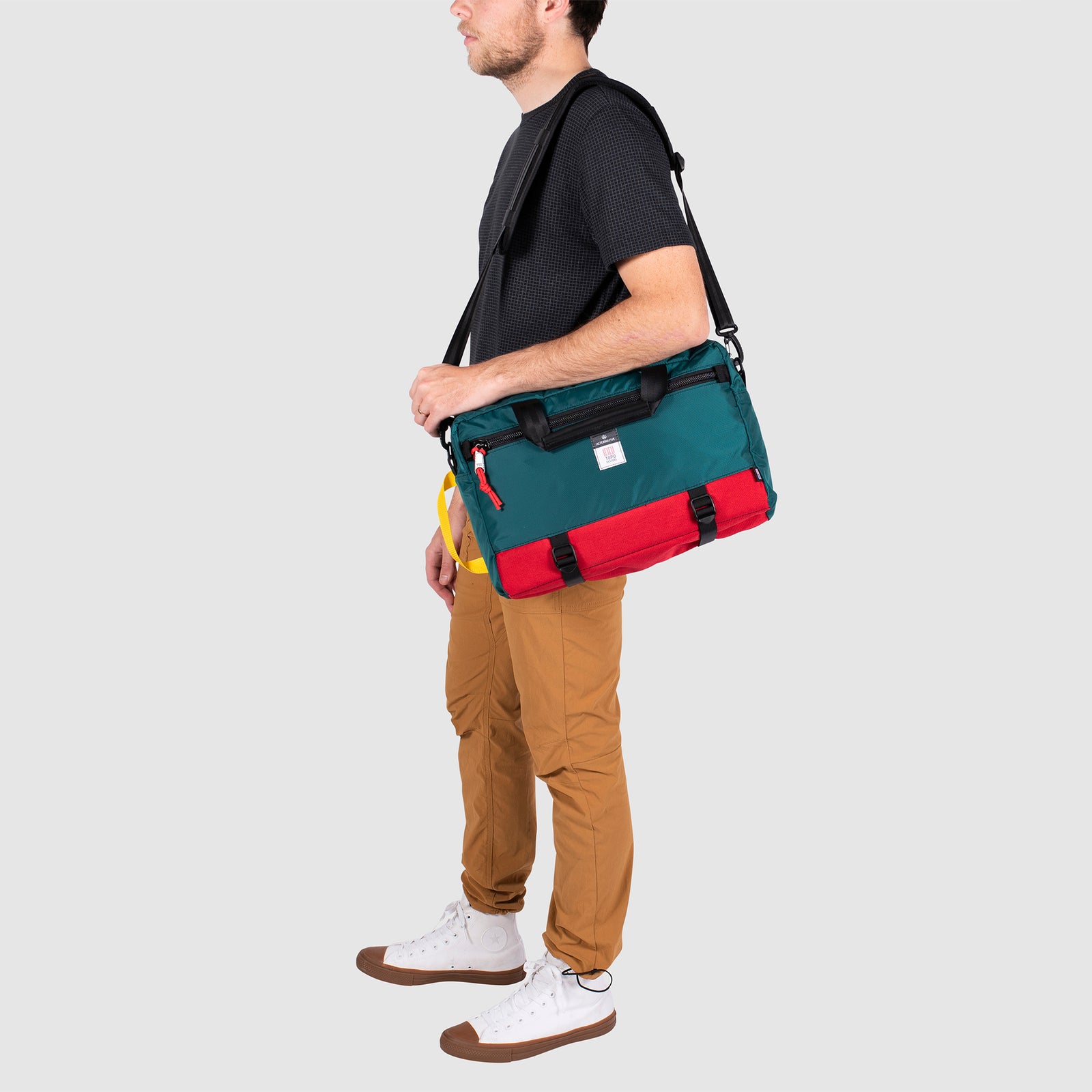 Model shot of Topo Designs x Alternative Commuter Briefcase in red/teal showing shoulder strap carry style