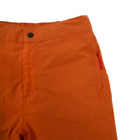 General front detail shot of Topo Designs Women's Lightweight Tech Pants in Brick orange showing waistband, fly, and zipper pulls on pockets.