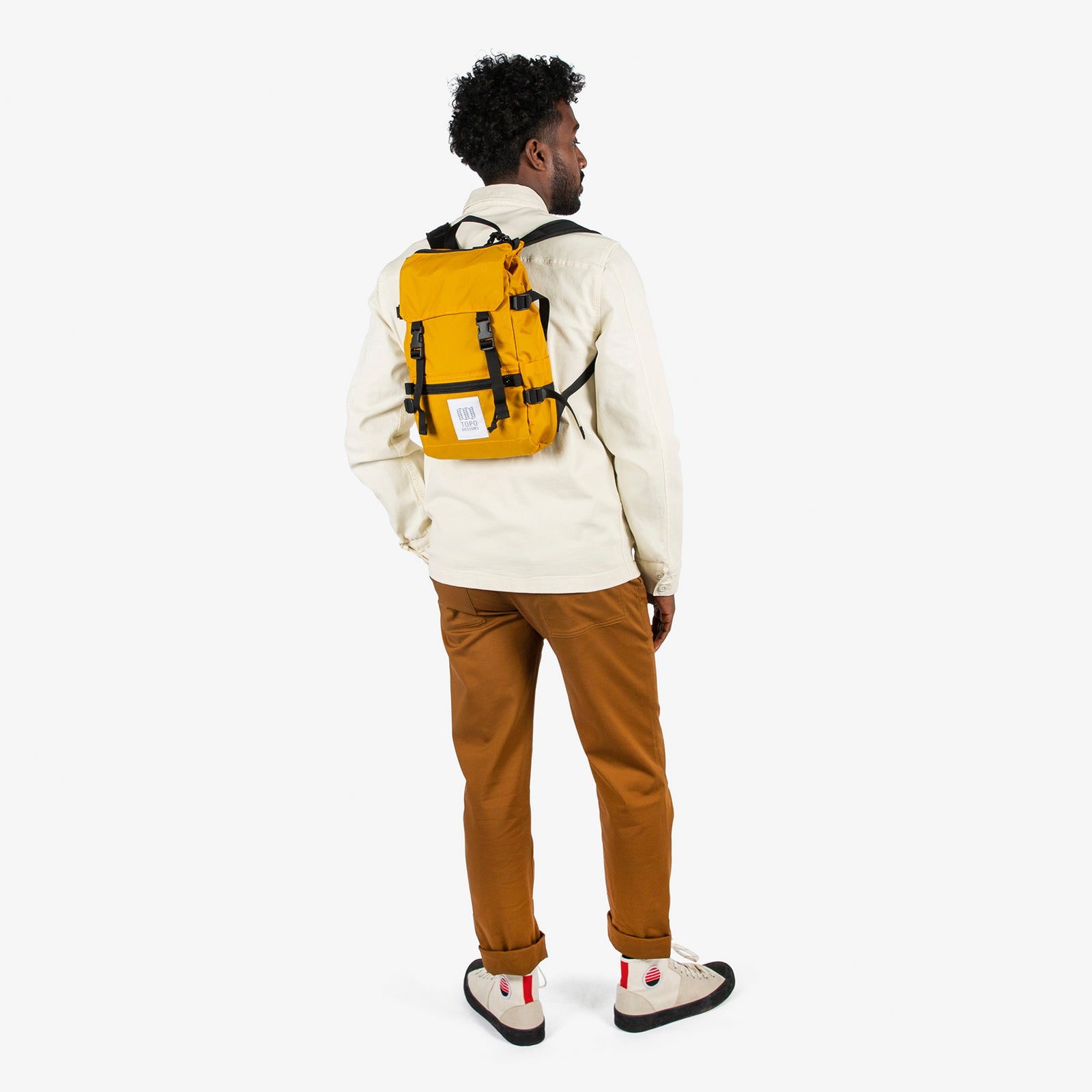 General shot of Topo Designs Rover Pack Mini backpack in "Mustard" yellow worn by model with backpack straps.