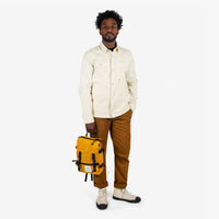 Topo Designs Rover Pack Mini backpack in "Mustard" yellow held by model with top carry handle.